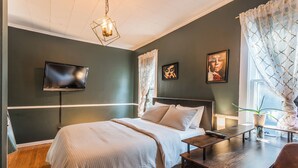 Ein modernes Schlafzimmer mit Bett, Nachttisch, Fernseher und Bildern an den Wänden.