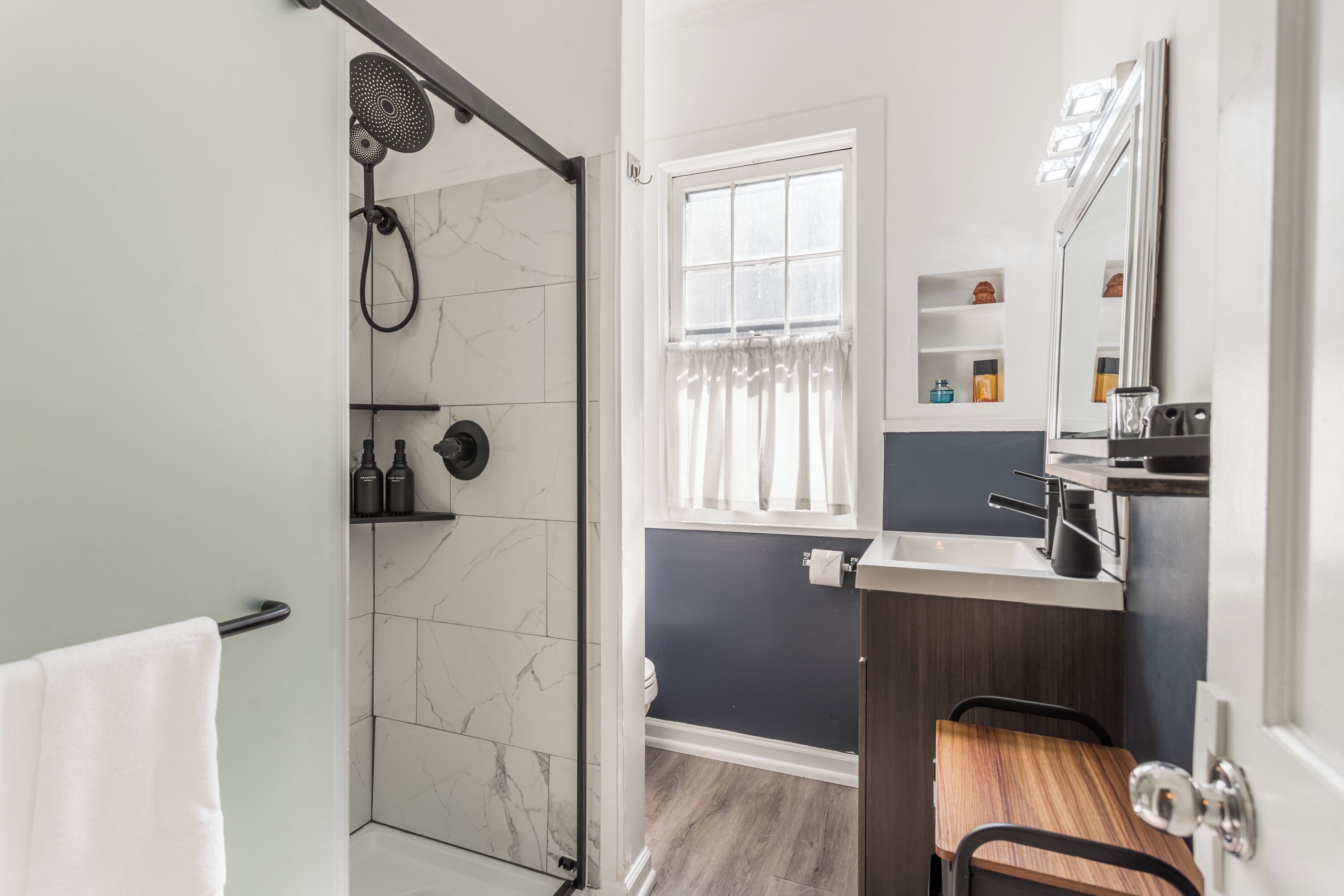 Un baño moderno con ducha, tocador con espejo y ventana.