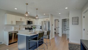 Una cocina moderna con gabinetes blancos, electrodomésticos de acero inoxidable y una isla central con taburetes de bar.