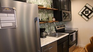 A compact kitchen with a stainless steel refrigerator, a coffee maker, a sink, and dark cabinets. - Jungle Boogie in Mountains (Cool Ridge)