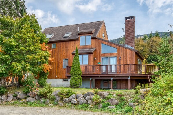 Une maison moderne en bois, dotée d’un balcon, de grandes fenêtres et d’une cheminée.