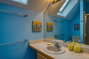 Une salle de bain avec un puits de lumière, un lavabo, un miroir et deux tableaux accrochés au mur.