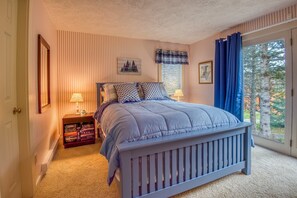 Une chambre à coucher avec un lit, une table de chevet, une fenêtre avec des rideaux et une vue sur les arbres à l’extérieur.