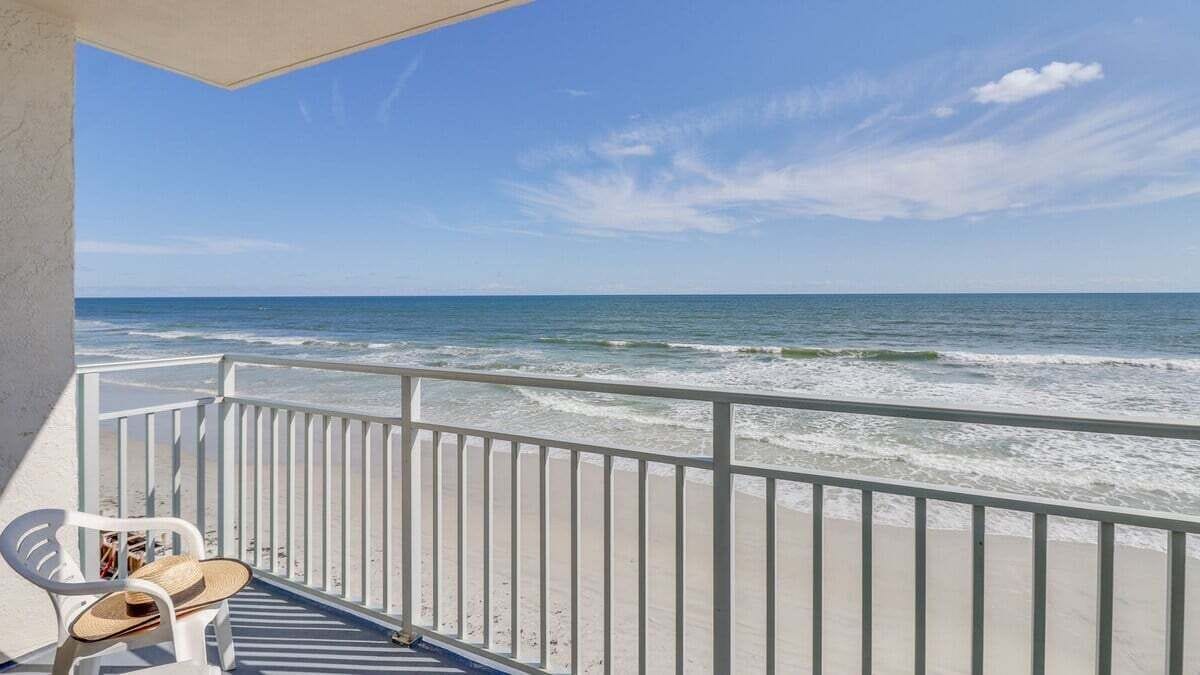 A balcony with a view of the ocean, a white railing, and a chair.
