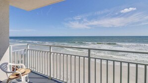 Een balkon met uitzicht op de oceaan, een witte balustrade en een stoel.