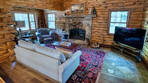L’intérieur d’une cabane en rondins, avec une cheminée en pierre, un téléviseur, un canapé et un tapis à motifs.