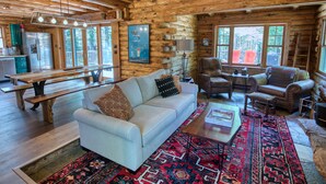 L’intérieur d’une cabane en rondins, avec un canapé blanc, un banc en bois, un tapis à motifs et une table à manger.