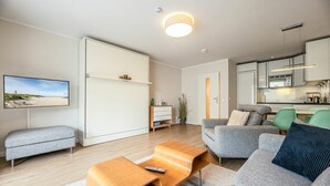 A modern living room with a sofa, a coffee table, and a TV on the wall. - Malin Haus Eydum - 2 room apartment in Haus Eidum. (Sylt)