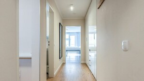 A hallway with wooden flooring, white walls, and a door leading to a bedroom with a bed and window. - Malin Haus Eydum - 2 room apartment in Haus Eidum. (Sylt)
