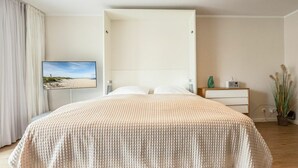 A bedroom with a bed, a TV on the wall, a nightstand, and a plant. - Malin Haus Eydum - 2 room apartment in Haus Eidum. (Sylt)