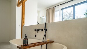 A modern bathroom with a freestanding bathtub, a wooden tray, and a bottle of shampoo. - Casa Terra Uluwatu (Pecatu)