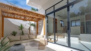 A modern outdoor living area with a sofa, a wicker chair, and a stone planter. - Casa Terra Uluwatu (Pecatu)