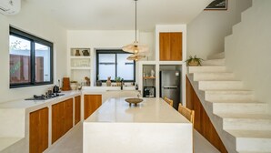 A modern kitchen with a central island, wooden cabinets, and a staircase. - Casa Terra Uluwatu (Pecatu)