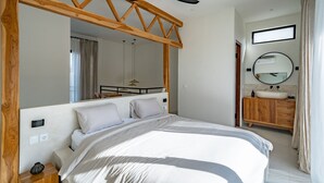 A bedroom with a bed, wooden headboard, ceiling fan, and a bathroom with a sink and mirror. - Casa Terra Uluwatu (Pecatu)
