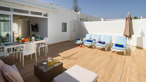 Patio esterno luminoso con tavolo da pranzo, sedie, poltrone relax e un tavolino con bevande.