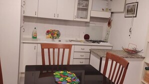 A compact kitchen with white cabinets, a gas stove, and a dining table with chairs. - LOCRI Epizephiri - Apartment 3 pl - Very close to the sea  (Locri)