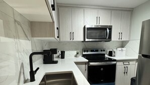 Una cocina moderna con armarios blancos, un lavamanos de acero inoxidable, un microondas, un horno y un refrigerador.