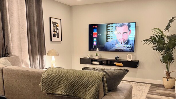 Un salón moderno con un sofá gris, un televisor de pantalla plana montado en la pared, una mesita auxiliar y una planta en maceta.