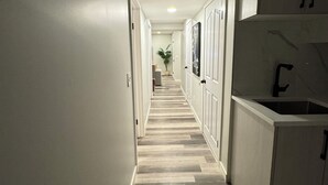 Un pasillo estrecho con suelo de madera, paredes blancas y una zona de cocina con armarios y un lavamanos.