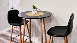 Una pequeña mesa redonda con una planta en maceta, dos sillas negras y una puerta blanca al fondo.