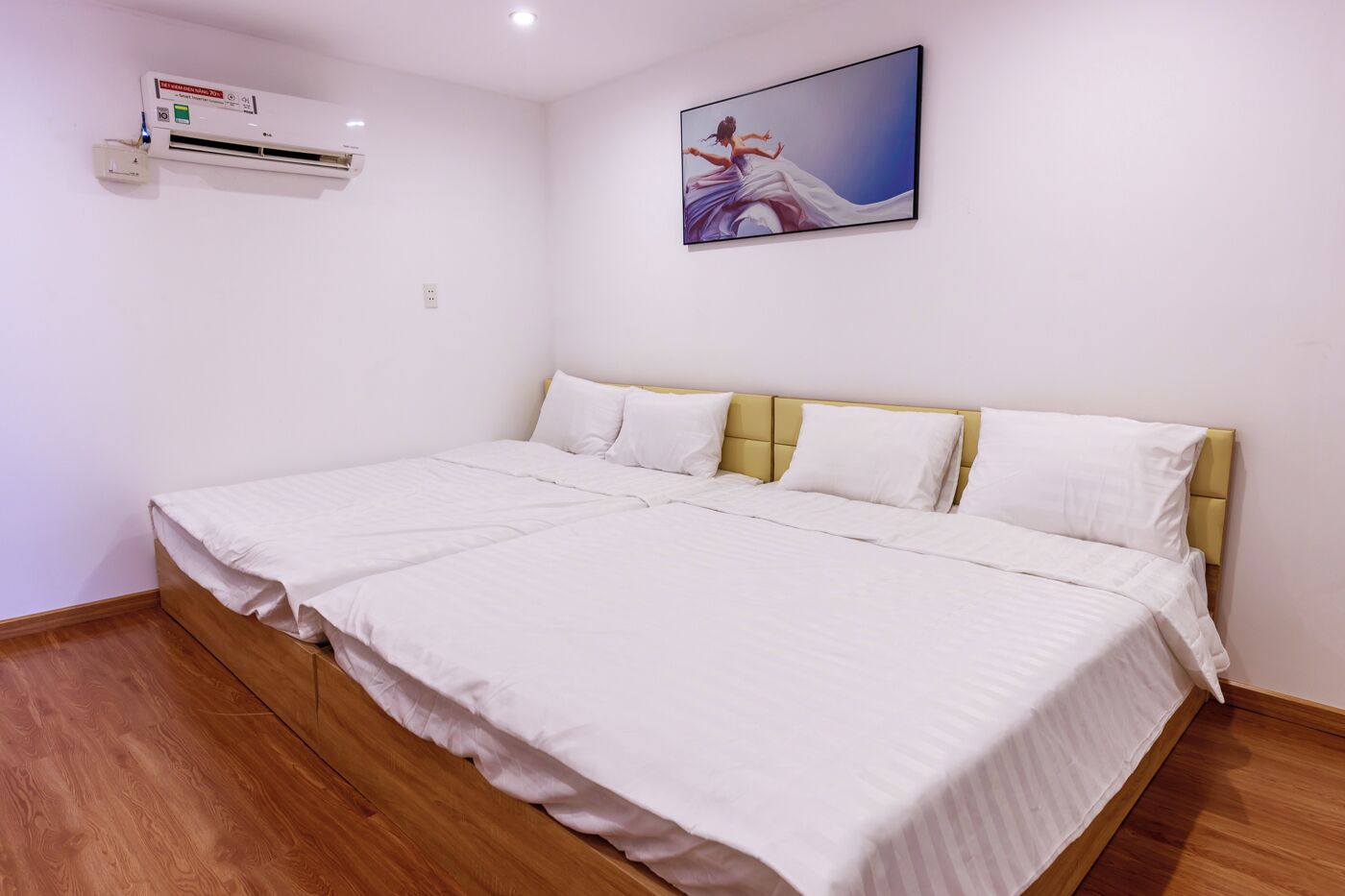 A bedroom with a large bed, white bedding, a yellow headboard, and a wall-mounted air conditioner.