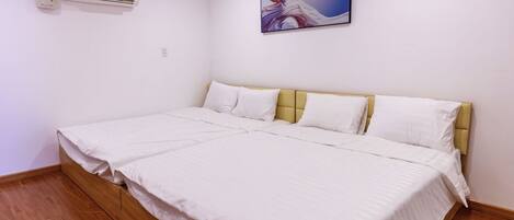 A bedroom with a large bed, white bedding, a yellow headboard, and a wall-mounted air conditioner.