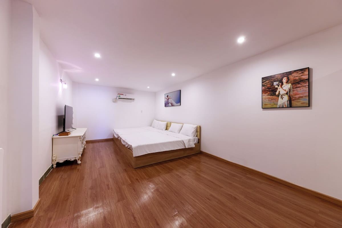 Un dormitorio con suelo de madera, una cama, un televisor sobre una consola blanca y un aire acondicionado en la pared.