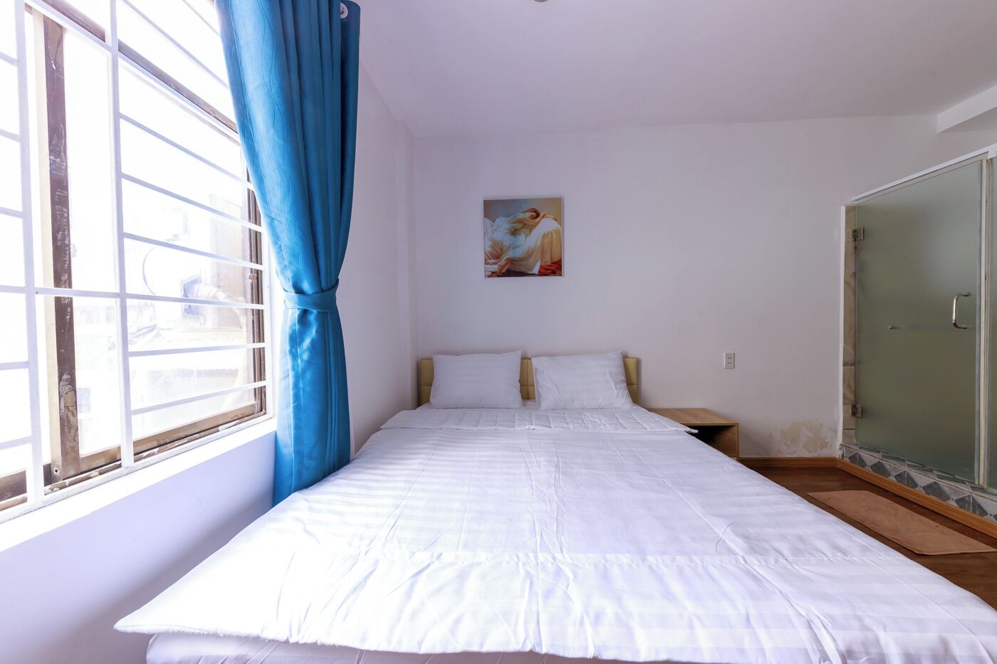 A bedroom with a bed, a painting on the wall, and a sliding glass door.