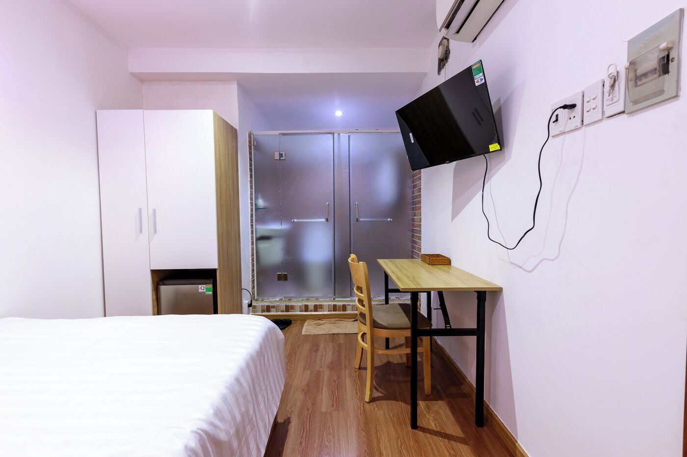 Ein Hotelzimmer mit Bett, Schreibtisch, Stuhl, einem an der Wand befestigten Fernseher und einem Kleiderschrank.