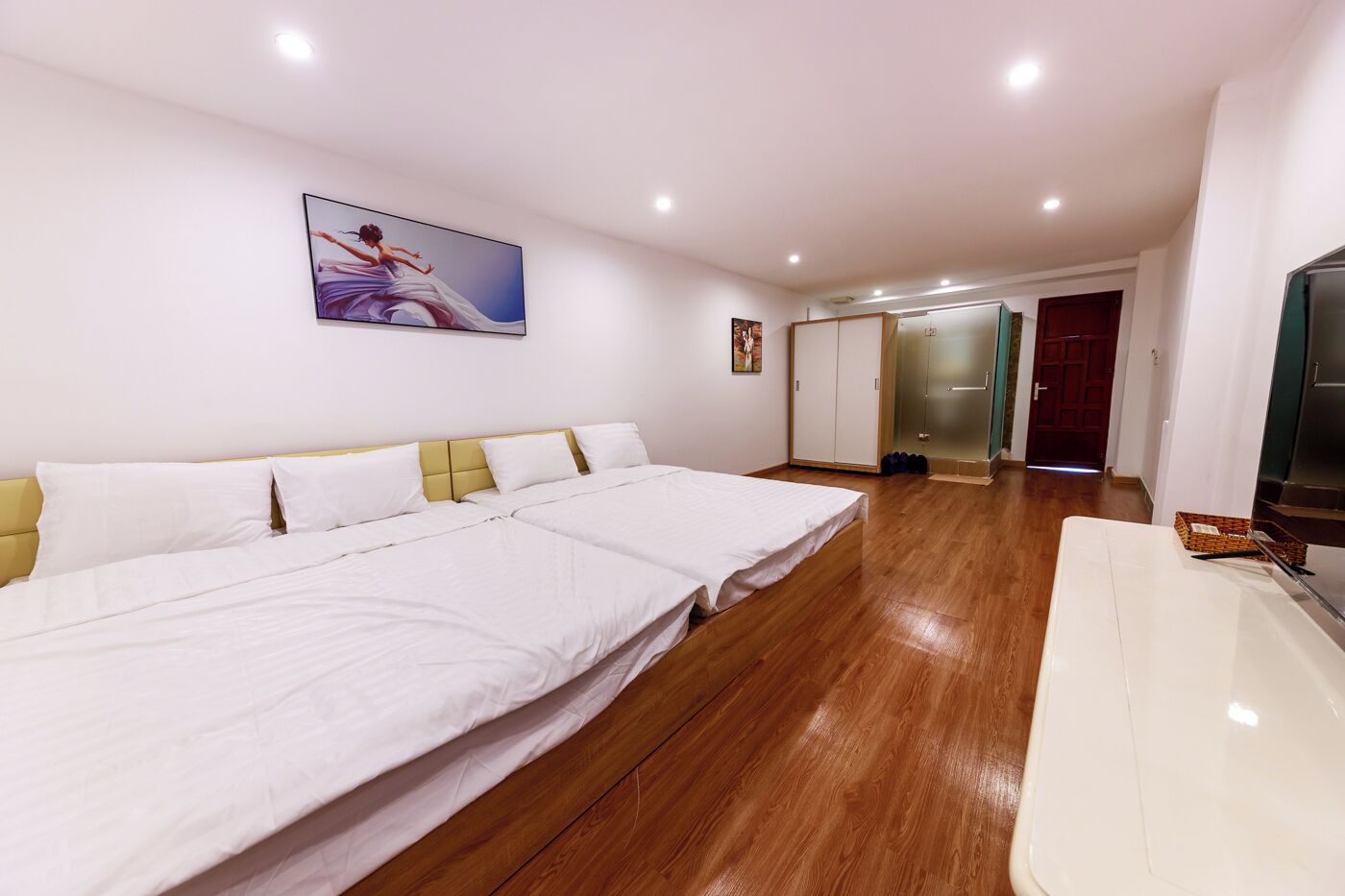 Habitación de hotel con una cama grande, televisión, suelo de madera y puerta que da a un baño.