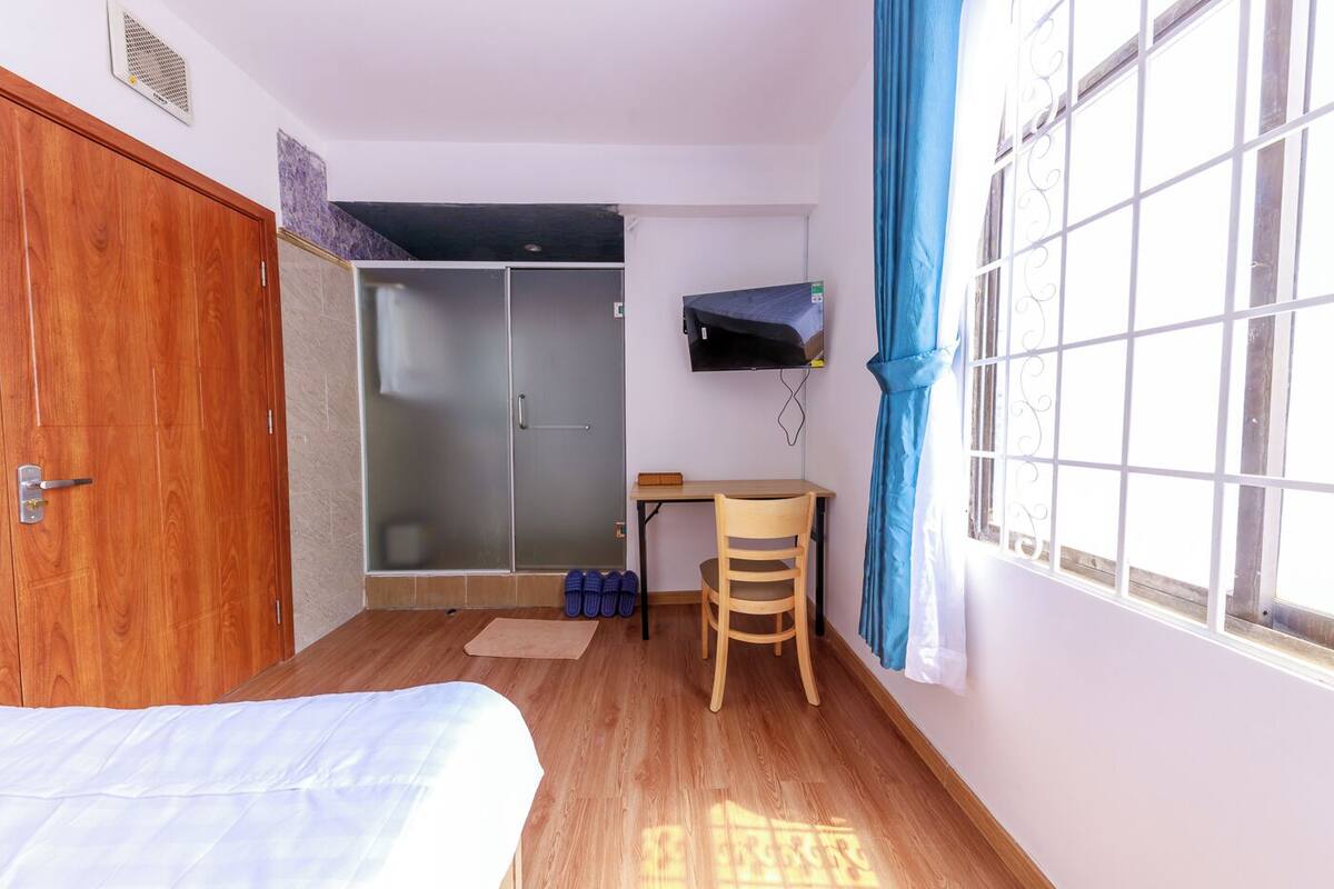Un dormitorio con cama, escritorio, silla, armario, puerta corredera y ventana con cortinas.