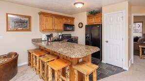 A kitchen with wooden cabinets, a granite countertop, a stainless steel refrigerator, and a bar stool seating area. - 3-bedroom condo in fabulous Eden, skiing, biking, hiking, and water sports (Eden)