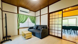 Una habitación con sofá, una pequeña mesa de madera, una lámpara de pie y una puerta corredera que da a otra estancia.