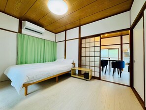 A traditional Japanese-style room with a wooden bed, a futon, a sliding door leading to a dining area, and an air conditioning unit. - Kawakunokaze⁂Entire Private Villa (Nishimuro District, Shirahama)