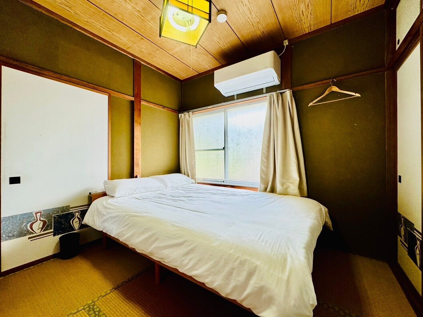 Un dormitori amb un llit, una finestra amb cortines, aire condicionat i un sostre de fusta.