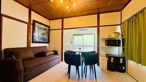 Un espacio habitable compacto con un sofá, dos sillones, una mesita, un cuadro enmarcado, un accesorio de iluminación en el techo y un microondas en un estante.