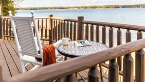 Une terrasse en bois avec une chaise blanche et une table ronde, donnant sur un lac.