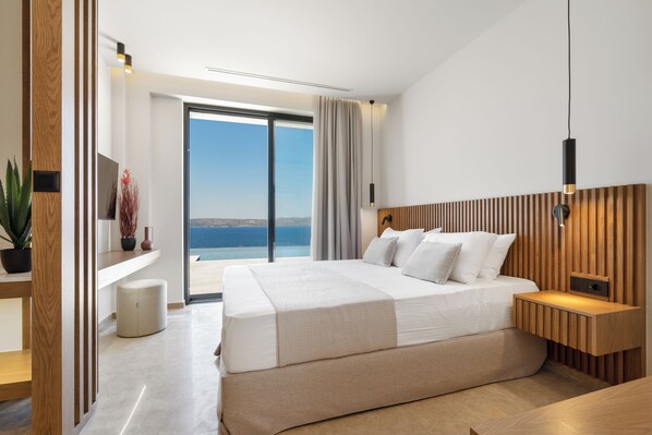 Una camera d'albergo moderna con un letto grande, una testiera in legno, un comodino, una pianta in vaso e vista sul mare.