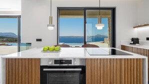 Eine moderne Küche mit einer großen Kochinsel, Holzschränken und Blick aufs Meer.