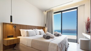 Ein modernes Hotelzimmer mit einem großen Bett, einem Holzkopfende, einem Nachttisch und Meerblick durch ein großes Fenster.