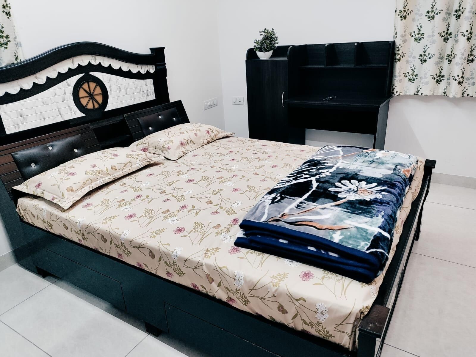 A bed with a floral bedspread, a decorative headboard, and a bedside table with a plant.
