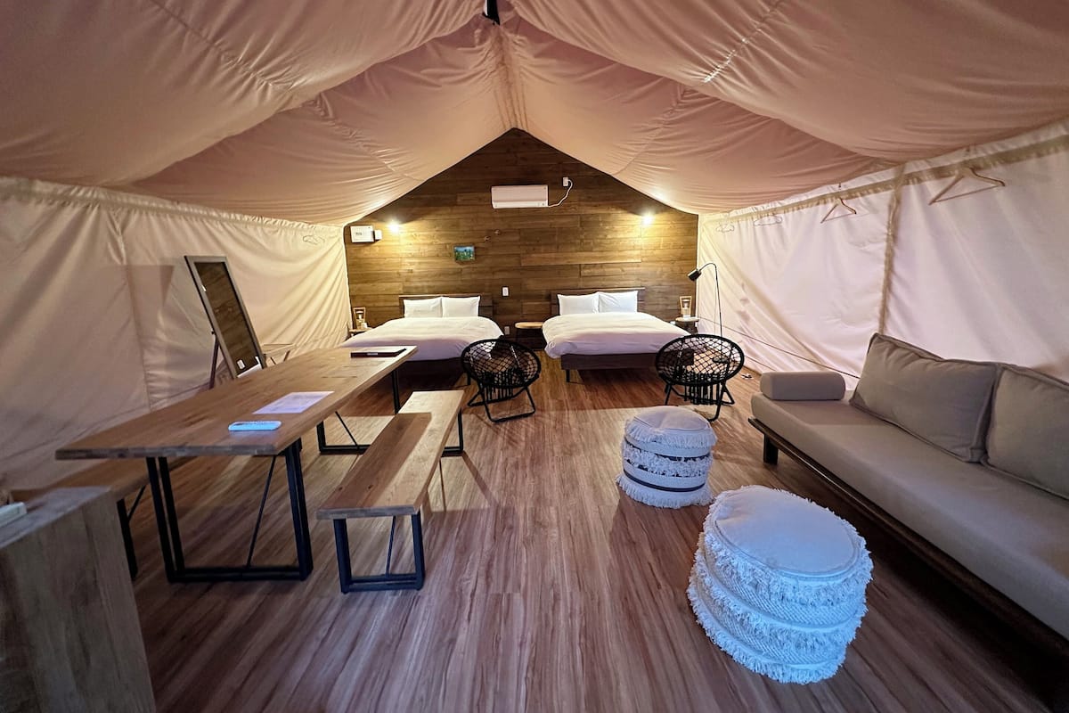 A tent-style room with two beds, a wooden floor, a table, a bench, and a sofa.