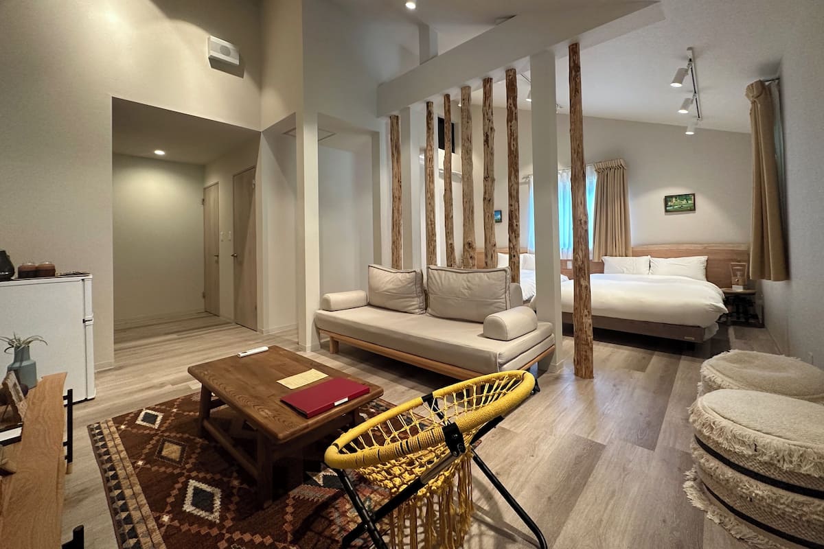 A modern hotel room with a sofa, a bed, a coffee table, a chair, and a small table with a lamp.