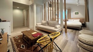Een moderne hotelkamer met een bank, een klein tafeltje, een gele geweven stoel, een bed en een houten scheidingswand.