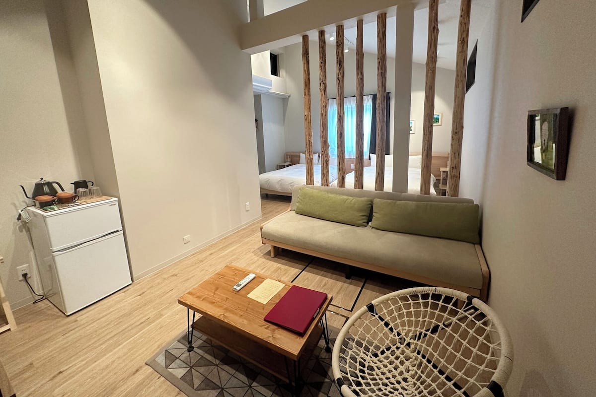 A modern room with a sofa, a wooden coffee table, a chair, and a small kitchenette.