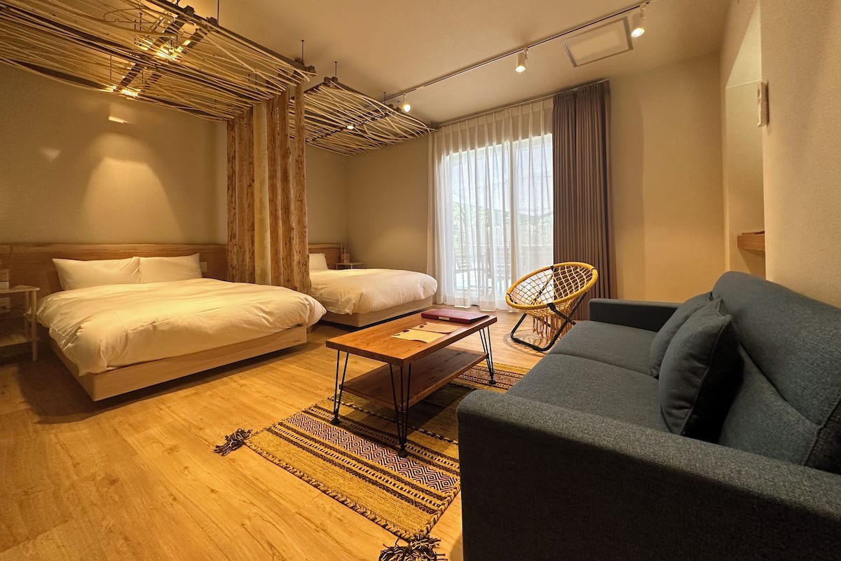 A hotel room with two beds, a sofa, a wooden coffee table, and a patterned rug.