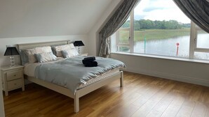Ein Schlafzimmer mit großem Fenster, einem Bett, einem Nachttisch und einer Lampe.