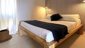 Un lit simple avec un cadre en bois, du linge de lit blanc et un plaid noir.