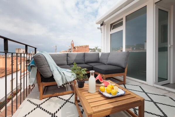 A balcony with a sofa, a table with fruits and a bottle, and a potted plant.