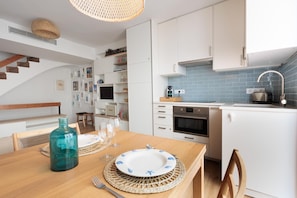 A modern kitchen with white cabinets, a blue tiled backsplash, and a wooden dining table set with plates and glasses.